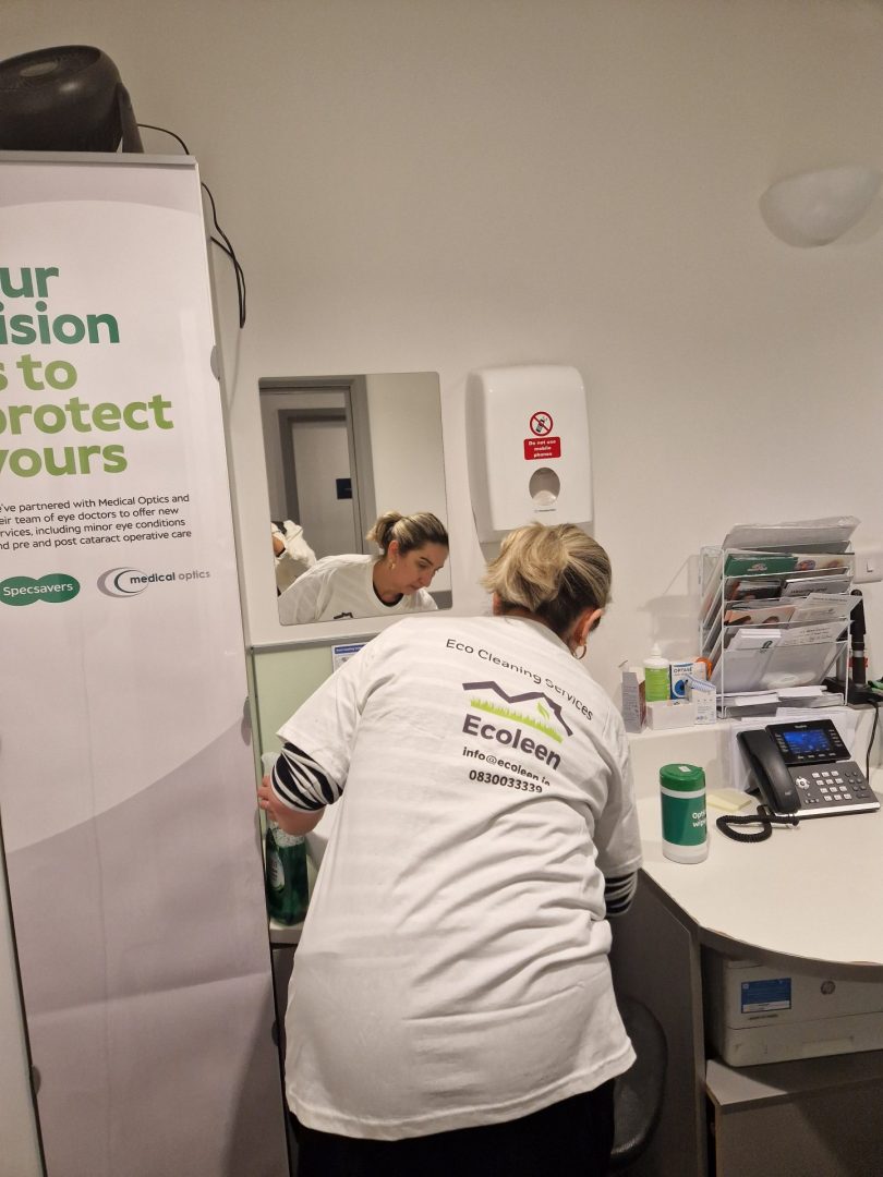 An Ecoleen cleaner in uniform cleaning a reception desk