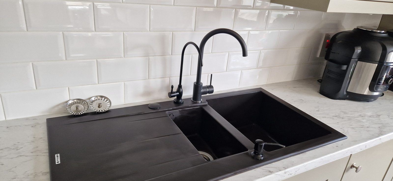 Clean black kitchen sink with white tiles behind it