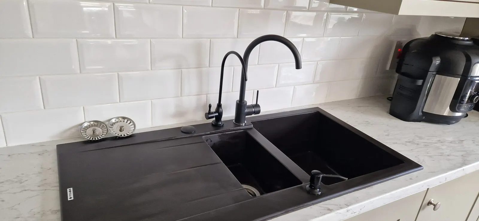 Clean black kitchen sink with white tiles behind it