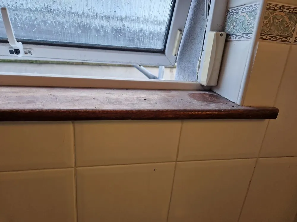 Bathroom window sill before cleaning, with water marks and dust on the wood