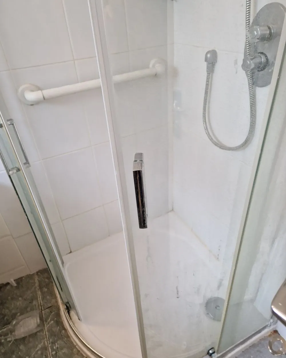 Shower enclosure before cleaning, with limescale and soap marks on the glass and tray
